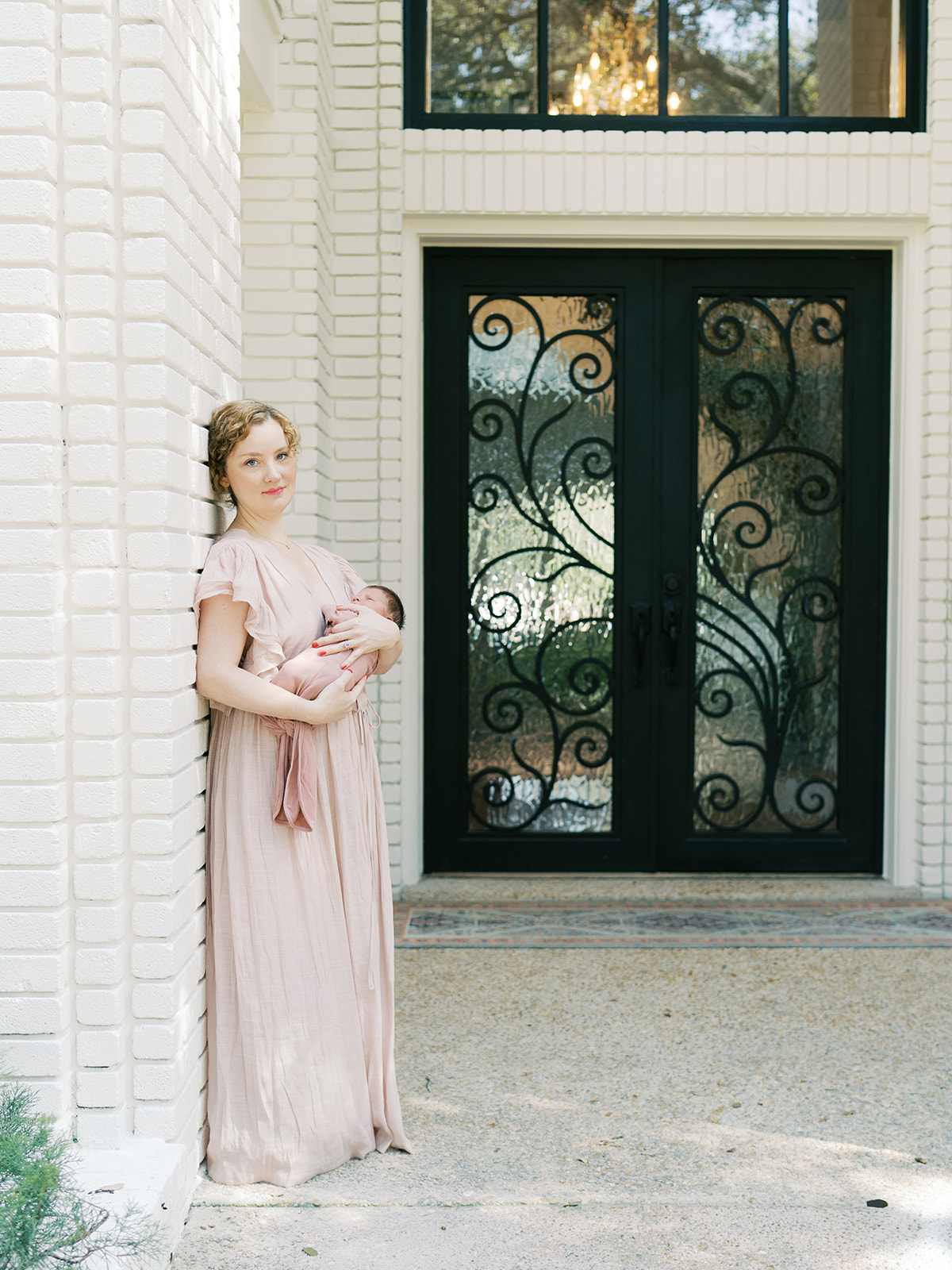 mom leans against entryway of home with newborn in arms