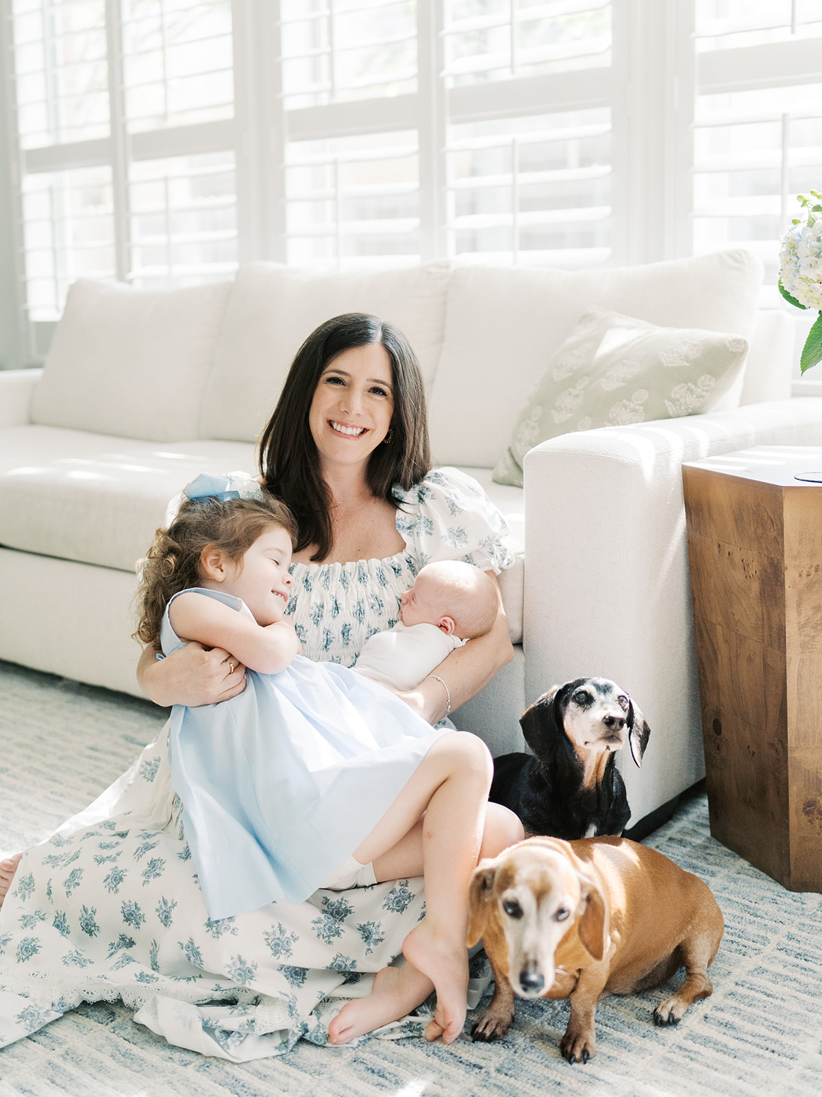 mom holds newborn and toddler girl with two dogs sitting nearby