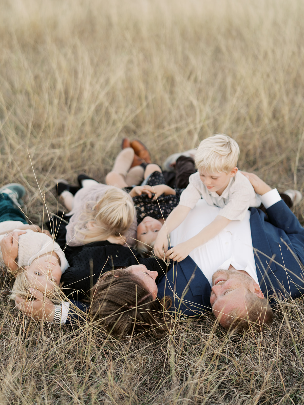 family of six lays in field of tall grass together 
